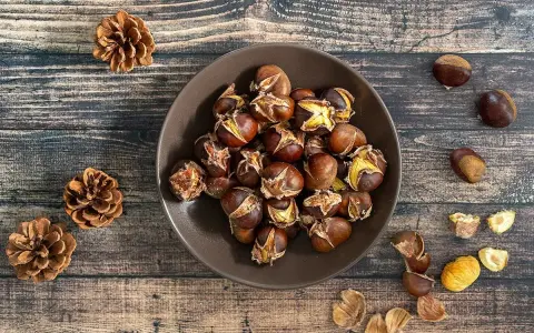 Châtaignes grillées dans un bol, sur fond de bois, avec des pommes de pin.