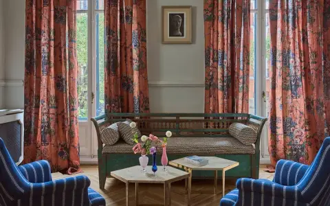 Cortinas de lino estampado con motivos florales y botánicos en tonos anaranjados, complementando un sofá vintage y sillones a rayas.