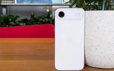 Biały iPhone z 4 aparatami, leżący na drewnianym blacie obok doniczki.