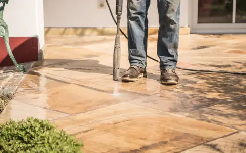 Nettoyer carrelage extérieur noirci avec un nettoyeur haute pression. L'eau projetée révèle la beauté naturelle des dalles.