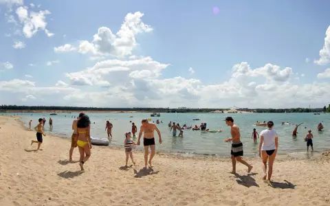 Menschen genießen einen sonnigen Tag am Badesee Frankfurt. Kinder planschen im Wasser, während Erwachsene sich am Sandstrand entspannen.