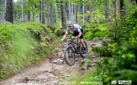 Kolarz MTB pokonuje kamienisty zjazd w lesie. To fragment kalendarza MTB, pełnego adrenaliny i pasji.