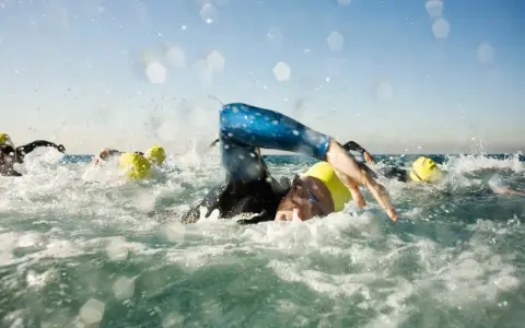 Schwimmer mit gelben Kappen kämpfen sich durch die Wellen. Die triathlon strecken sind anspruchsvoll.