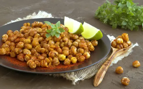 Ceci croccanti al forno, conditi con paprika e guarniti con basilico fresco e spicchi di lime, invitano a uno snack salutare e gustoso.
