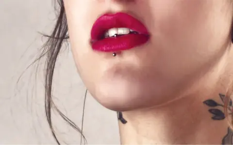 Usta z czerwoną szminką i ashley piercing. Delikatny tatuaż na szyi dodaje uroku.