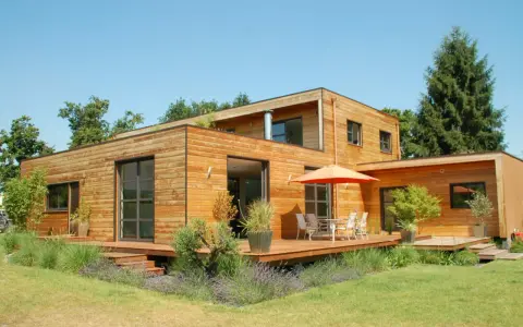 Maison moderne en bois avec terrasse et jardin. La construction maison ossature bois met en valeur le matériau naturel.