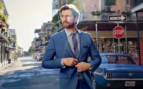 Man in a sharp blue suit, ready for a business cocktail, stands on a street with a vintage car and classic architecture.