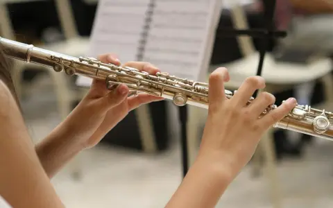 Dłonie grające na srebrnej flecie, jednym z tych mało znanych instrumentów muzycznych, na tle nut.