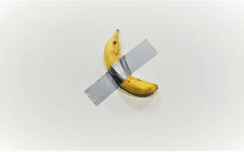 A ripe banana, a symbol of Maurizio Cattelan's art, is taped to a white wall.