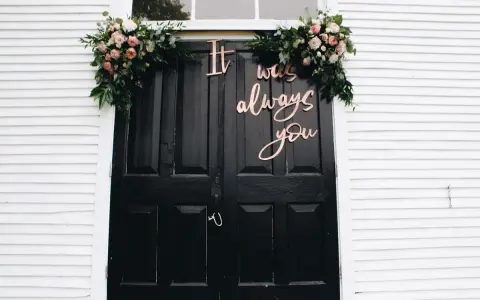 Elegancka dekoracja domu pana młodego: czarne drzwi ozdobione kwiatami i napisem "It was always you".