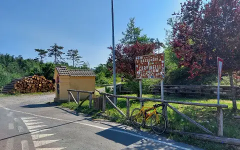 Bicicletta gialla appoggiata alla staccionata al Passo dei Carpinelli, con un cartello che indica l'altitudine e un piccolo edificio.
