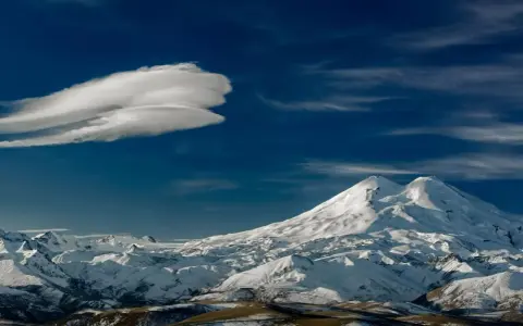 Elbrus szczyt w chmurach lenticularnych. Majestatyczne, ośnieżone góry pod błękitnym niebem.