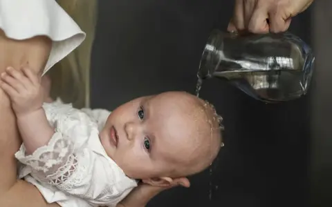 Chrzest chłopca: polewanie główki wodą z dzbanka.