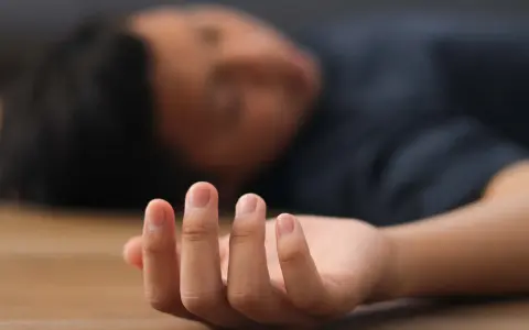Nahaufnahme einer Hand, die auf dem Boden liegt, während eine Person mit einem epileptischen Anfall bewusstlos ist.