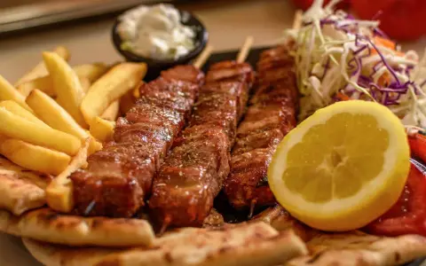 Pyszne souvlaki na patykach, podane z frytkami, pitą, surówką i cytryną.
