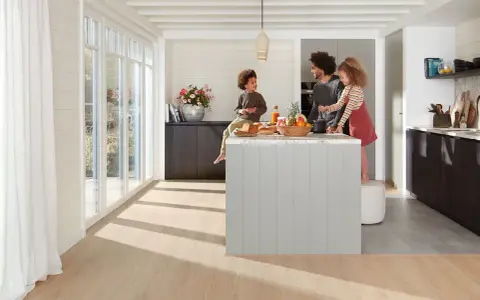 Une famille prépare un repas dans une cuisine moderne. La **délimitation sol cuisine salon** est subtile, avec un parquet clair contrastant avec le carrelage du salon.