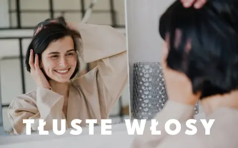 Uśmiechnięta kobieta dotyka swoich włosów, zastanawiając się, co zrobić, żeby włosy się nie przetłuszczały.