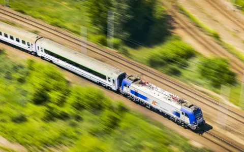 Pędzący pociąg PKP Intercity, model EU44 "Husarz", z białymi wagonami, mija zielone pola i drzewa.