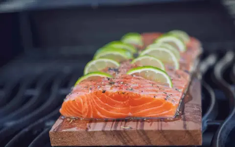 Lachs auf Zedernholz grillen, mit Limettenscheiben und Kräutern belegt. Ein saftiges Stück Fisch auf dem Rost.