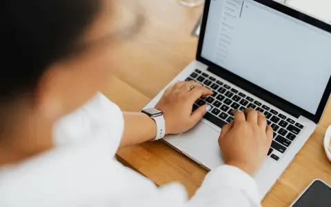Kobieta pisze na laptopie, na ekranie widać artykuł po niemiecku.