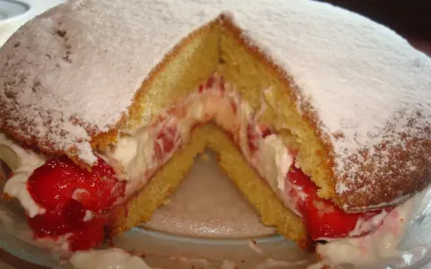 Puszysty biszkopt przełożony kremem i truskawkami, posypany cukrem pudrem. Klasyczny victoria sponge cake.