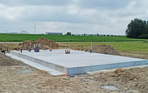 Płyta betonowa, czyli fundament, gotowa do budowy domu. Wokół piasek i zielone pola.
