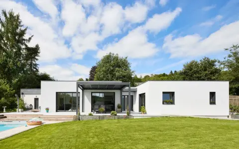Une maison modulable moderne avec piscine et jardin luxuriant, sous un ciel bleu éclatant.