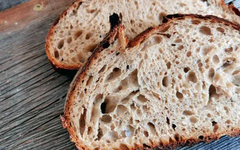 Zwei Scheiben rustikales Sauerteigbrot mit großer Porung liegen auf einem Holzbrett. Die Sauerteig Vorteile sind offensichtlich: ein toller Geschmack und eine bekömmliche Textur.