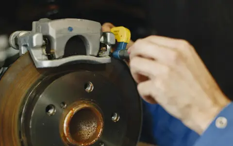 Mechanik dokręca śrubę w jarzmie zacisku hamulcowego, naprawiając układ hamulcowy pojazdu.