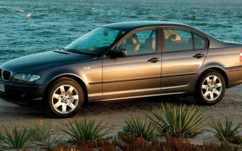 Szary sedan BMW E4 na plaży, z morzem w tle.
