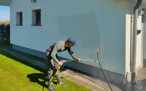 Mężczyzna myje elewację domu myjką ciśnieniową.