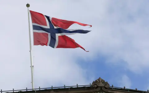 Norwegische Flagge weht im Wind über einem Gebäude. Die Diskussion über den Stromverbrauch in Norwegen ist aktuell.