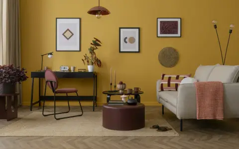 Un salotto con pareti giallo ocra e dettagli tortora. Un divano beige, un pouf tortora e un tappeto in juta creano un'atmosfera accogliente.