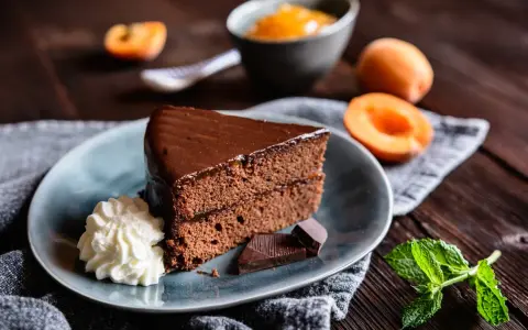 Ein Stück Sachertorte, das aussieht wie vom Original Sachertorte Rezept, mit Schlagobers, Schokolade und Marillenmarmelade.