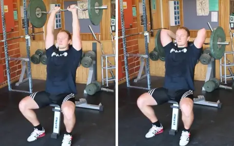 Man utför french press i gym. Han sitter på en bänk med en skivstång över huvudet, redo att sänka den bakom nacken.