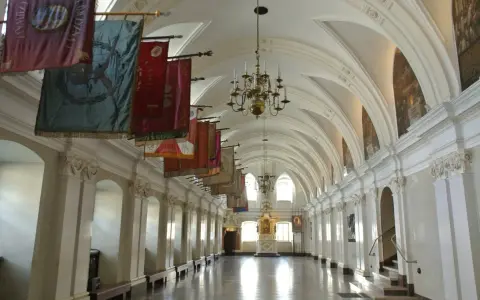 Długi korytarz z łukami i żyrandolami, ozdobiony historycznymi sztandarami. To wnętrze klasztoru na Jasnej Górze, gdzie każdy baner opowiada historię zakonu paulinów.