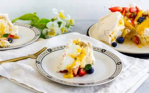 Porción de pavlova con fresas, arándanos y mango, bañada en salsa de maracuyá. Los pavlova ingredientes son visibles en este postre.