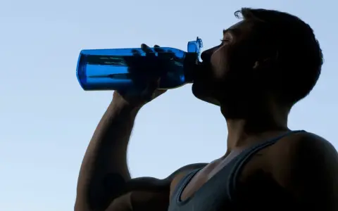 Mann trinkt aus blauer Flasche, erfrischt sich nach dem Sport.