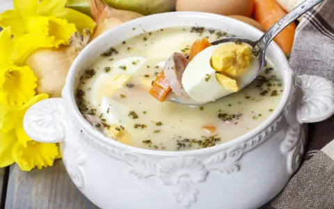 Biały barszcz z jajkiem i kiełbasą, w tle żonkile i cebula. Czym się różni żurek od barszczu białego? Ten pierwszy ma kwaśniejszy smak.