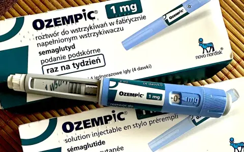 Dwa opakowania i dwa peny leku Ozempic 1 mg na podkładce bambusowej.
