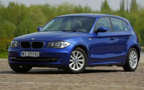 Błękitne BMW E87 z polskimi tablicami WI 3114J, z nowymi żarówkami w reflektorach, zaparkowane na bruku.
