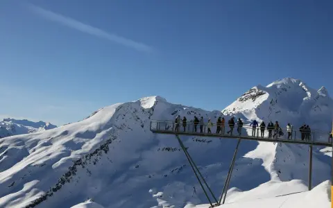 Ludzie na platformie widokowej podziwiają ośnieżone szczyty Alp, jakby byli w świecie Grindelwalda.
