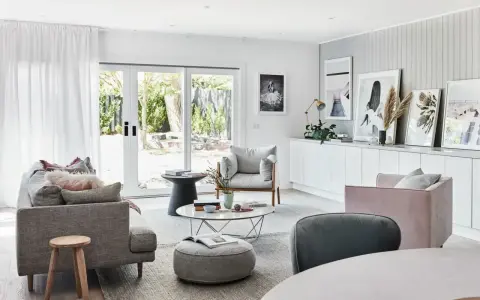 Elegante salón con sofás grises y rosas, mesa de centro y **cuadros apoyados en muebles** de la pared.