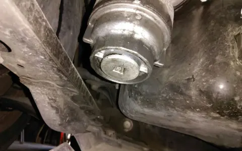 Filtre à huile de voiture sous le véhicule, avec une clé carrée insérée.