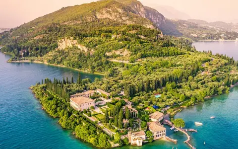 Punta San Vigilio: eine Villa mit Gärten und Zypressen am türkisfarbenen Gardasee, umgeben von grünen Hügeln.