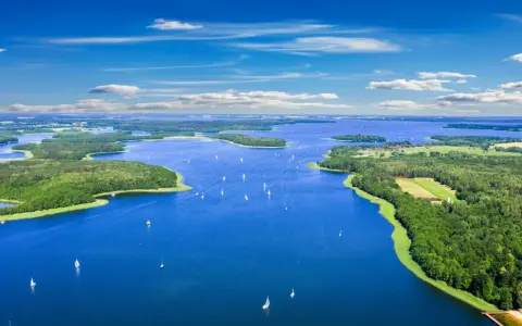 Malownicze mazury jeziora z licznymi wyspami i żaglówkami pod błękitnym niebem.