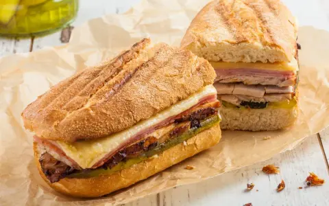 Dos sándwiches cubanos a la parrilla con capas de carne, queso derretido y pepinillos.