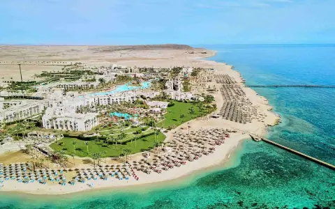 Albatros Palace Port Ghalib: rozległy kompleks hotelowy z basenami, palmami i plażą pełną leżaków, otoczony pustynnym krajobrazem i turkusowym morzem.