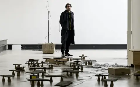 Tarek Atoui, artiste, se tient au milieu d'une installation sonore avec de nombreuses petites structures en pierre et en bois reliées par des câbles.