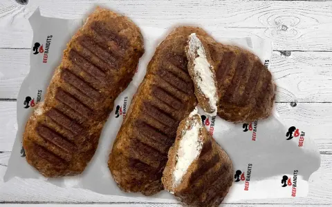 Gegrillte Bifteki, eines davon aufgeschnitten, zeigt eine cremige Füllung. Perfekt, um Bifteki selber machen zu lernen!